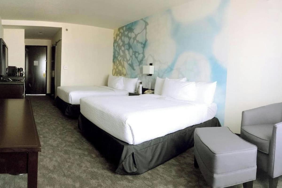 Une chambre d’hôtel avec deux lits, un bureau, une chaise et un tableau au mur.