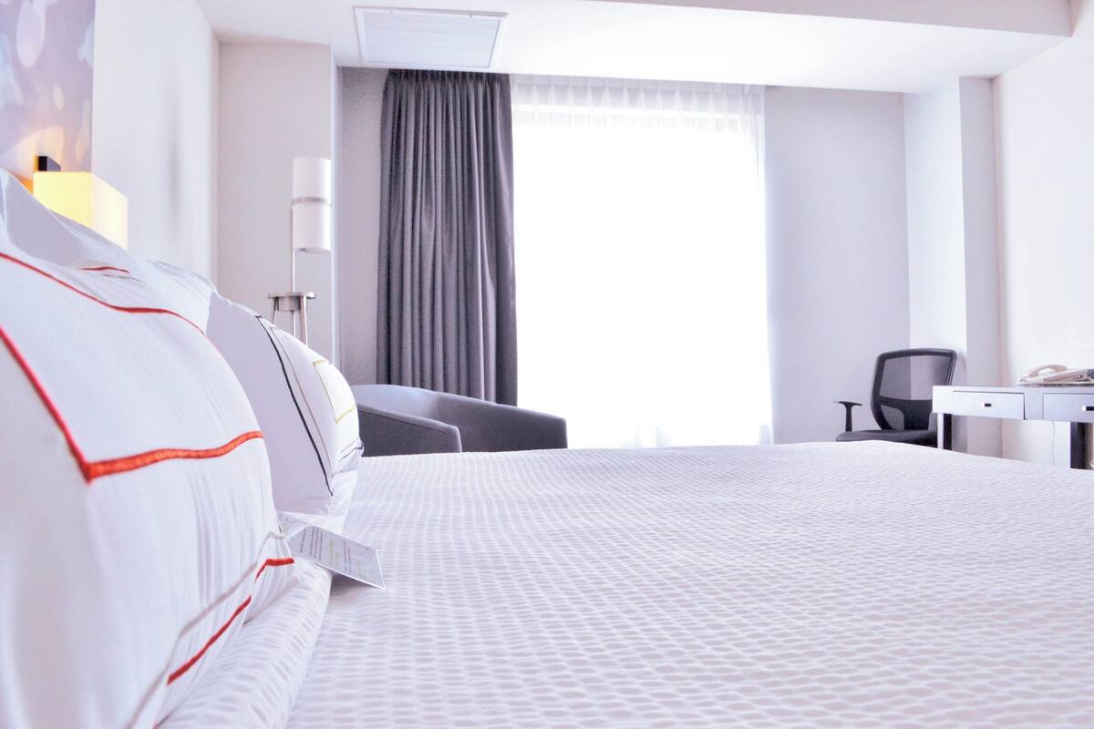 Une chambre d’hôtel avec un grand lit, un bureau, une chaise et une fenêtre avec des rideaux.