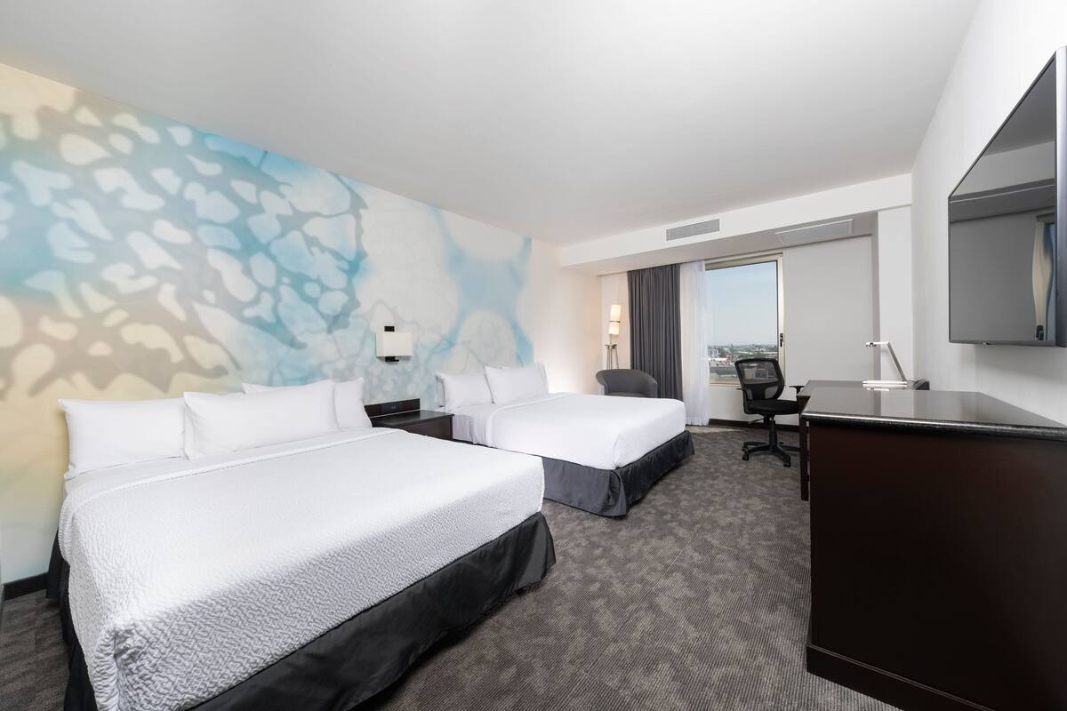 Une chambre d’hôtel avec deux lits, un bureau, une chaise, un grand miroir et une vue sur la ville.