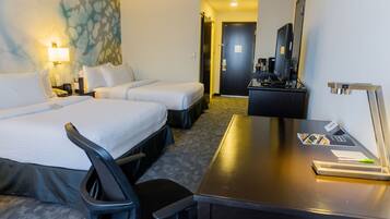 Quarto de hotel com duas camas, uma escrivaninha, uma cadeira, luminária de mesa, máquina de café e um espelho.