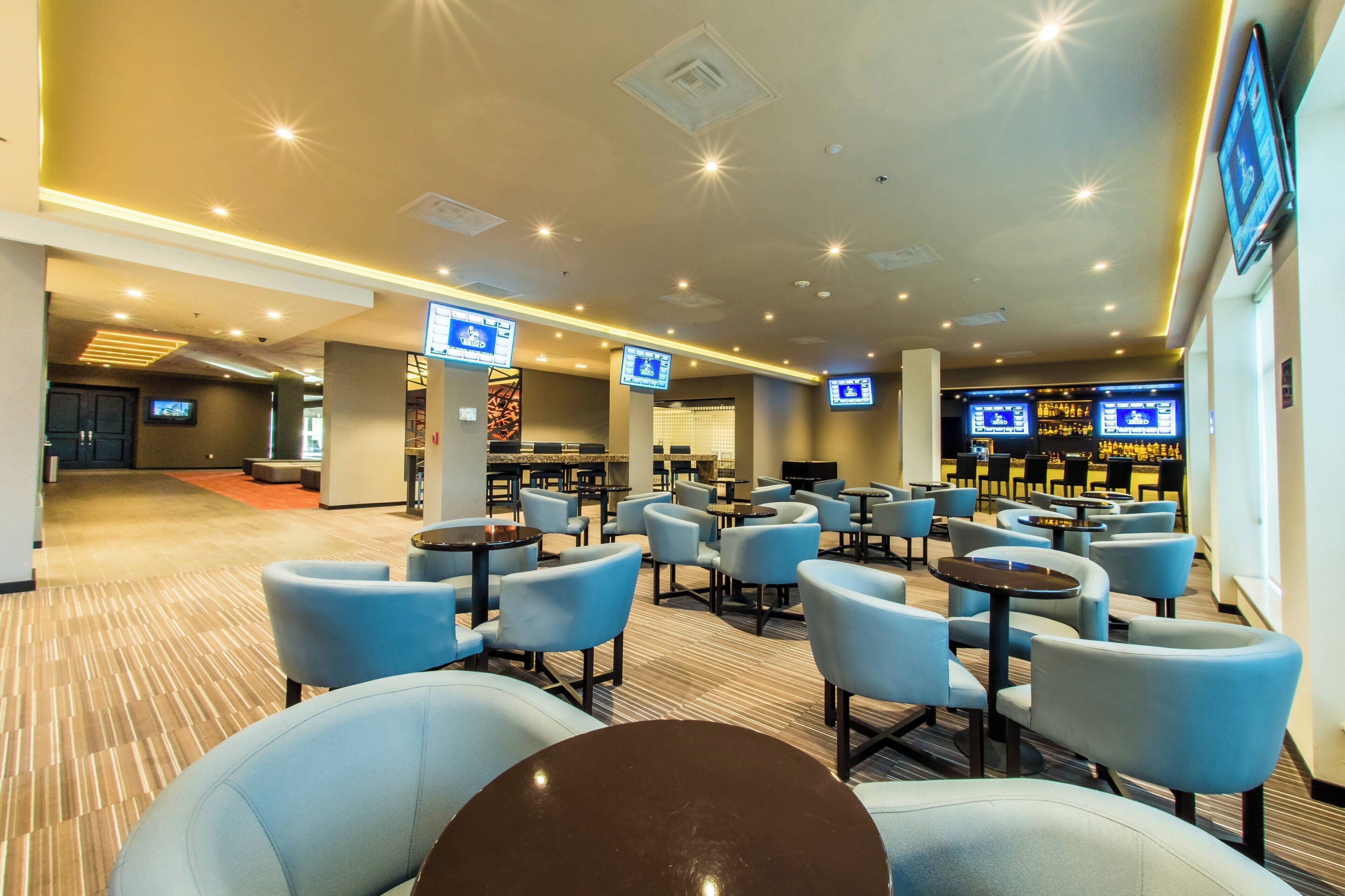 A hotel lobby with seating areas, a reception desk, and multiple screens displaying information.