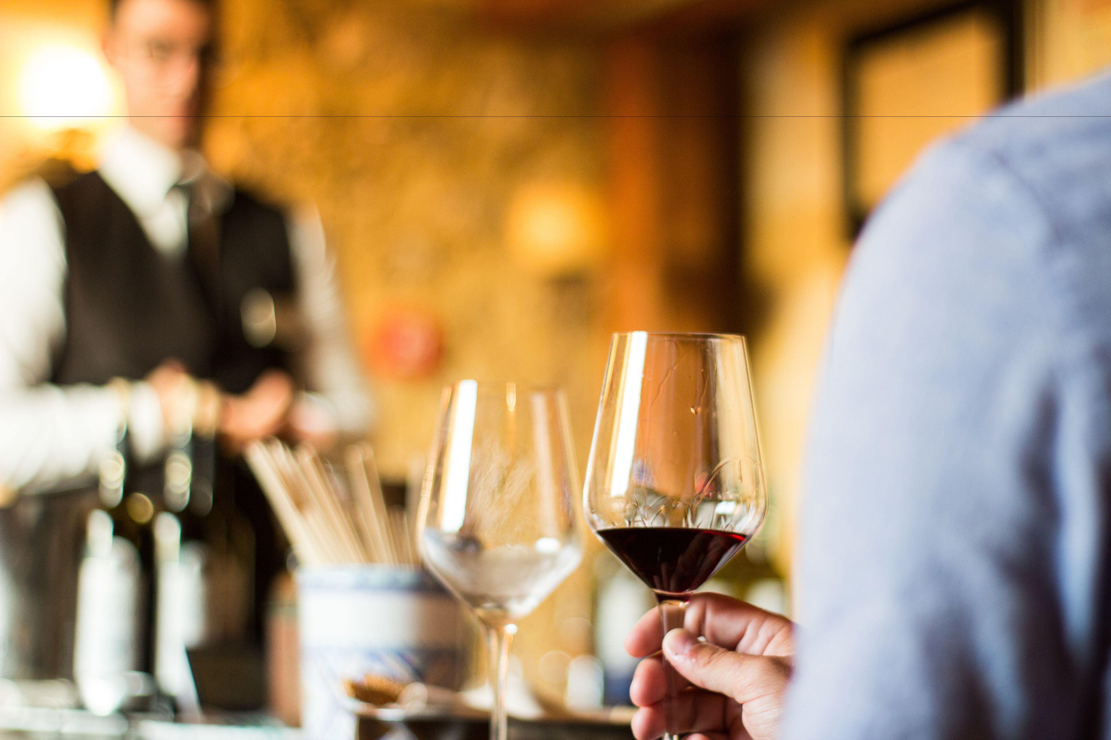 A bar setting with a focus on a hand holding a wine glass.