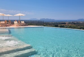 A clear blue pool with lounge chairs and umbrellas, surrounded by a fence, overlooking a coastal landscape. - Baglio Oneto dei Principi di San Lorenzo - Luxury Wine Resort (Marsala)