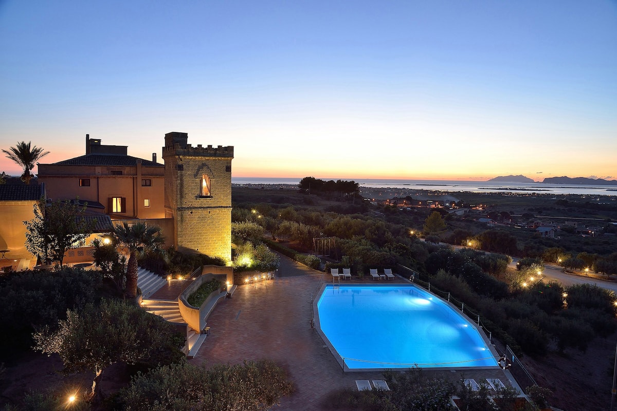 Zona junto a la piscina con vista despejada al mar, una torre y un atardecer.