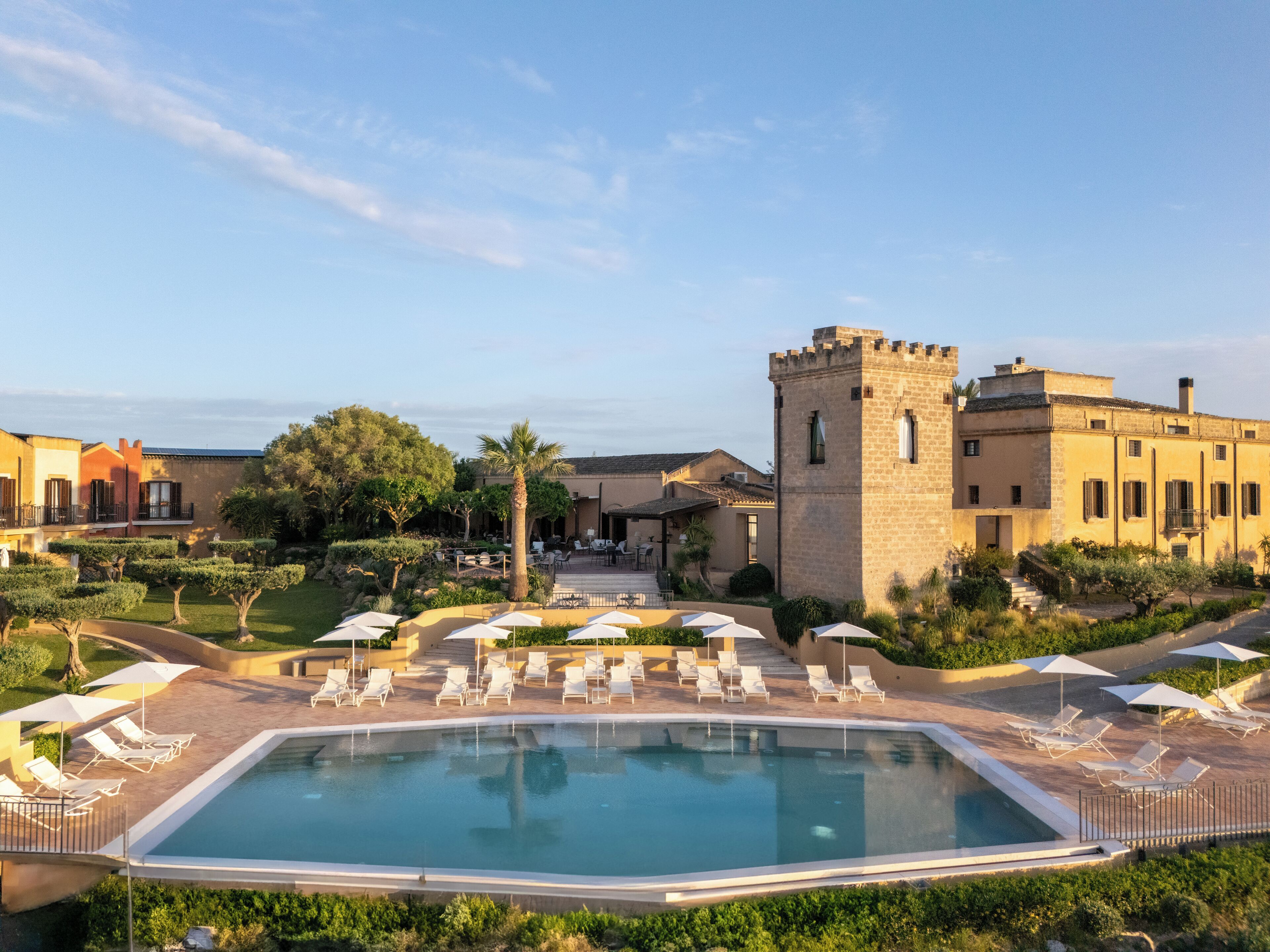 A pool area with lounge chairs and umbrellas, surrounded by buildings with a castle-like tower.