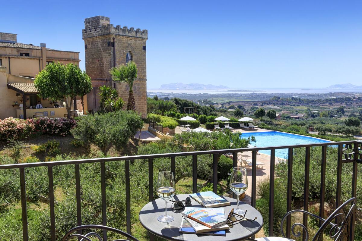 Un balcón con vista a un castillo, una piscina y abundante vegetación.