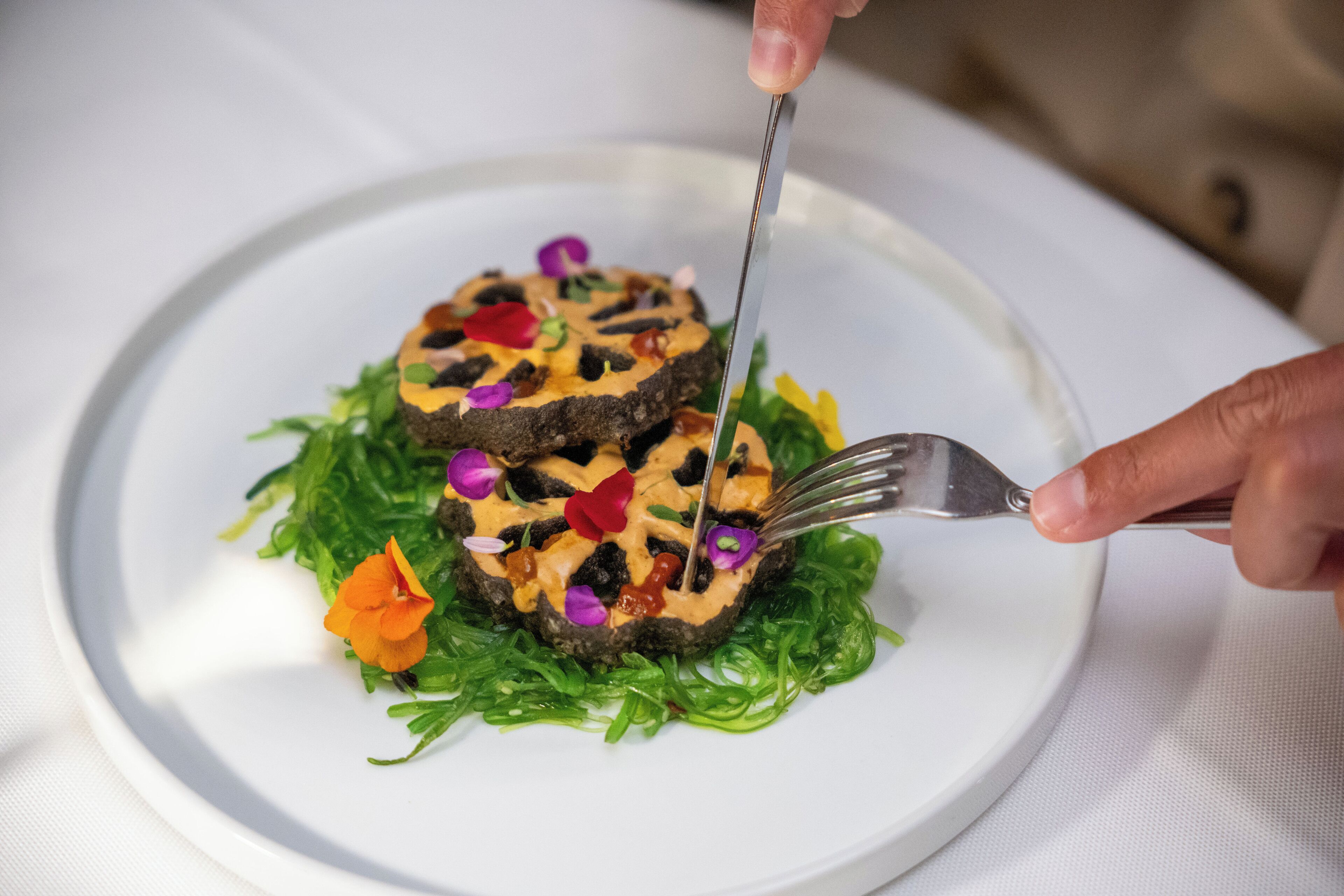 A plate with a food item, garnished with green leaves and colorful edible flowers.