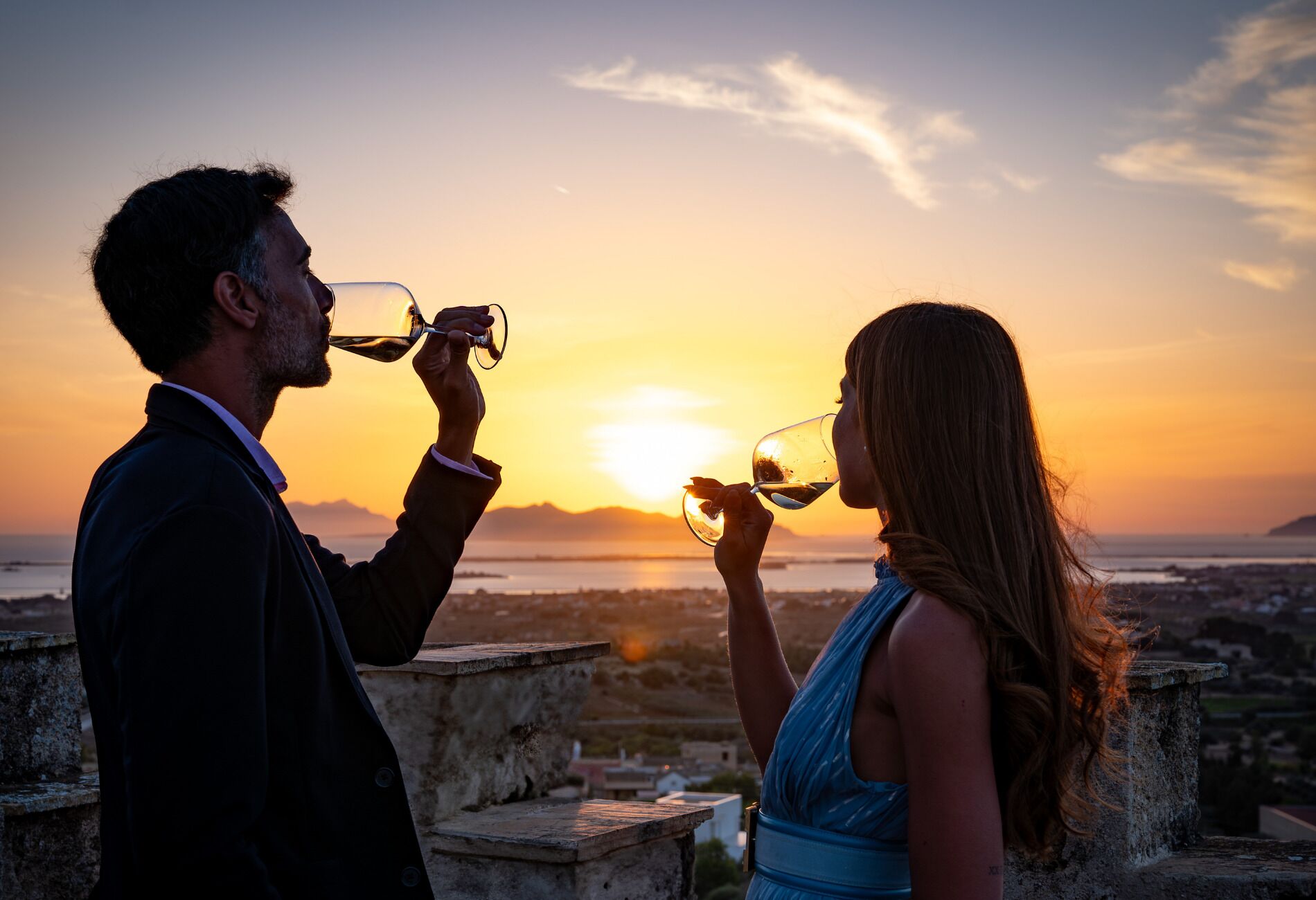 Two people toasting with wine glasses against a sunset backdrop.