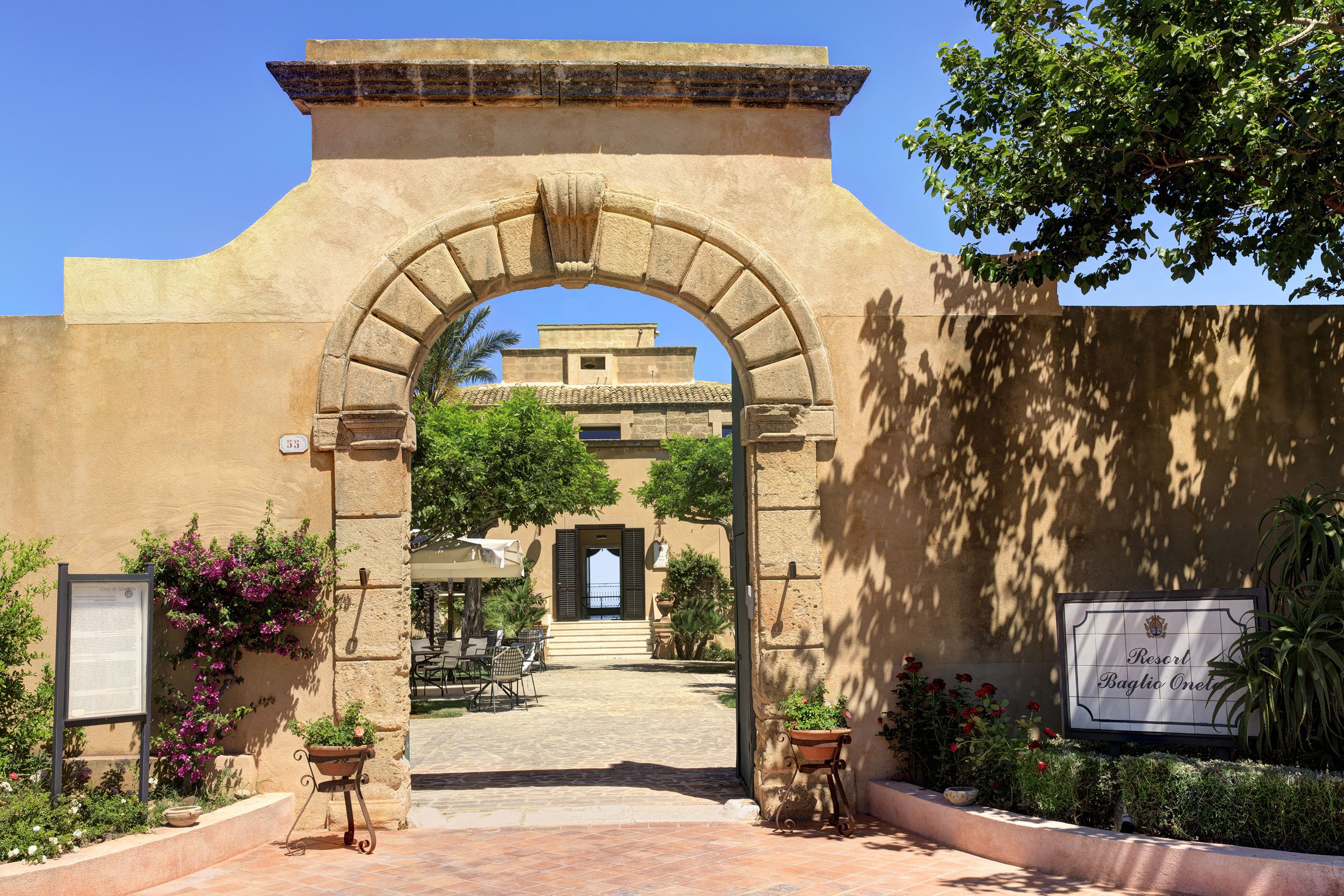 Un arco de entrada a un patio con mesas al aire libre y un cartel que indica Resort Baglio Orvieto.
