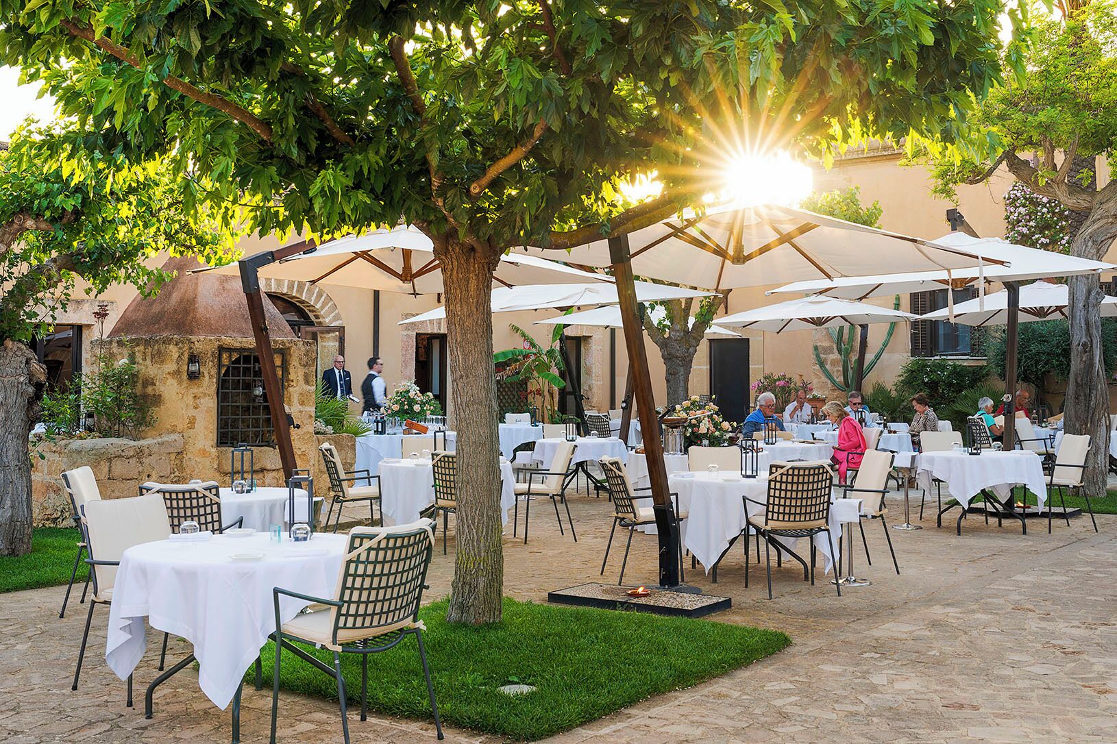 Un espace de restauration en plein air, avec des tables et des chaises, entouré d’arbres et abrité par des parasols.