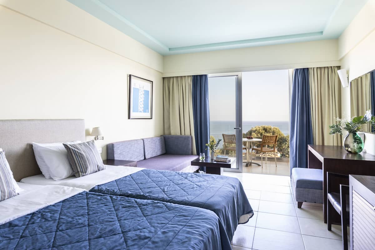 A hotel room with two beds, a sofa, a desk, and a balcony with a view.