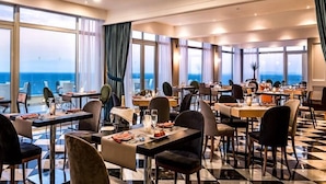 Un restaurante con piso a cuadros, mesas listas para cenar y grandes ventanales que ofrecen vista al mar.