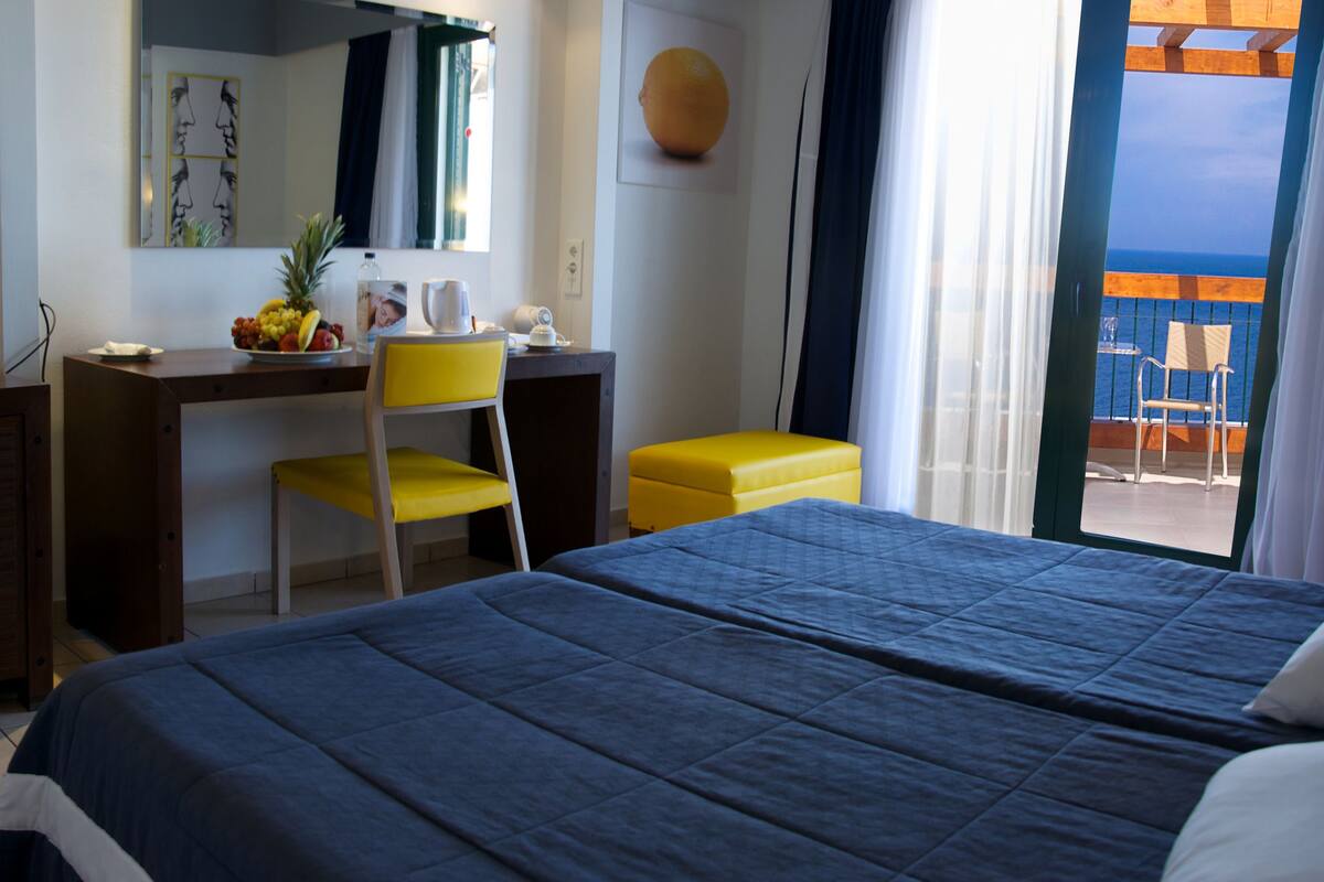 A hotel room with a bed, a desk with a chair, a television, and a view of the ocean.
