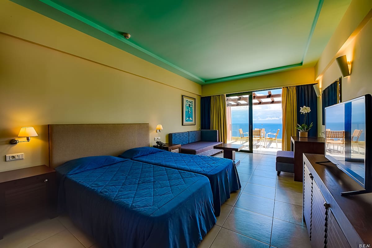 A hotel room with two beds, a desk, a TV, and a balcony with a view.