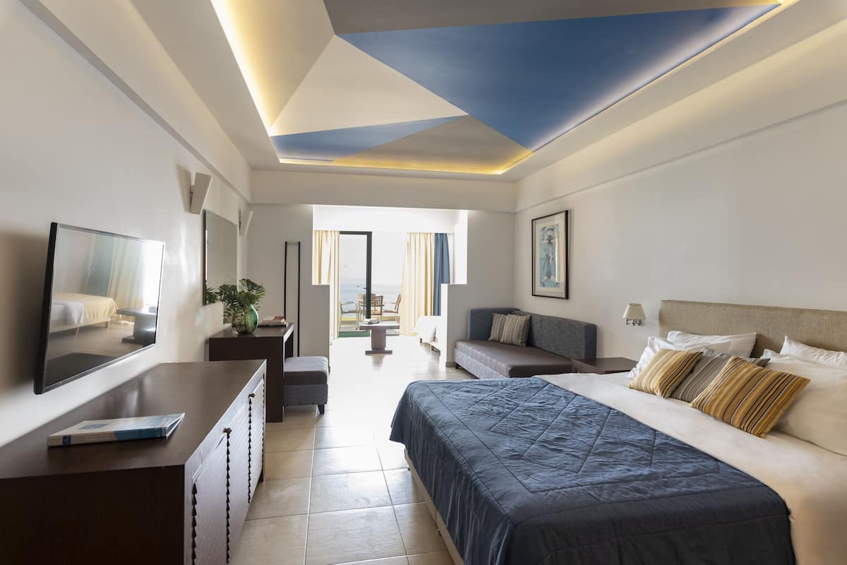 A modern hotel room with a large bed, a desk, a chair, and a view of the outdoors.