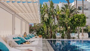 A poolside area with lounge chairs, a pool, and tropical plants.