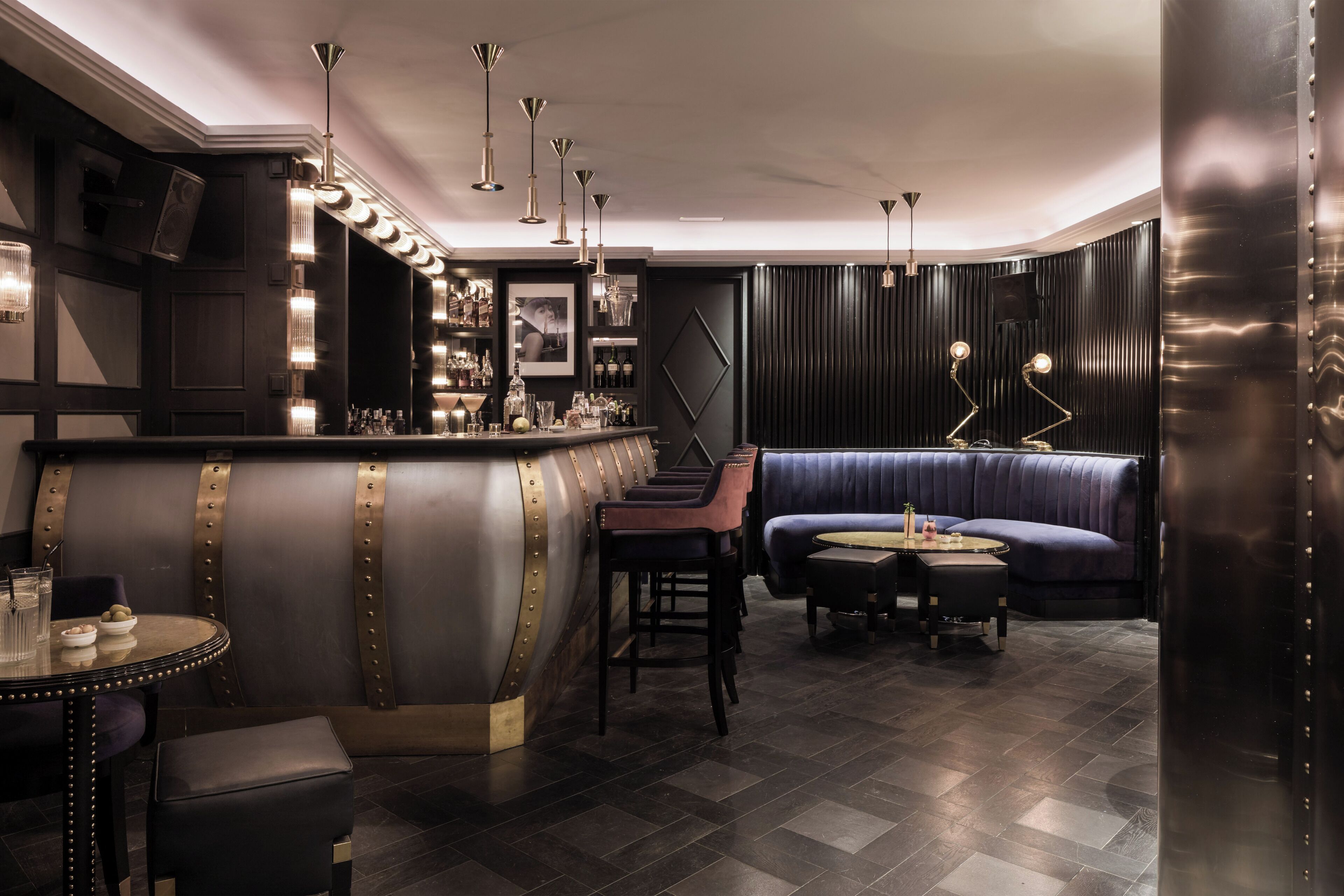 Een bar met een toonbank, barkrukken en een zithoek met een bank en ronde tafel.