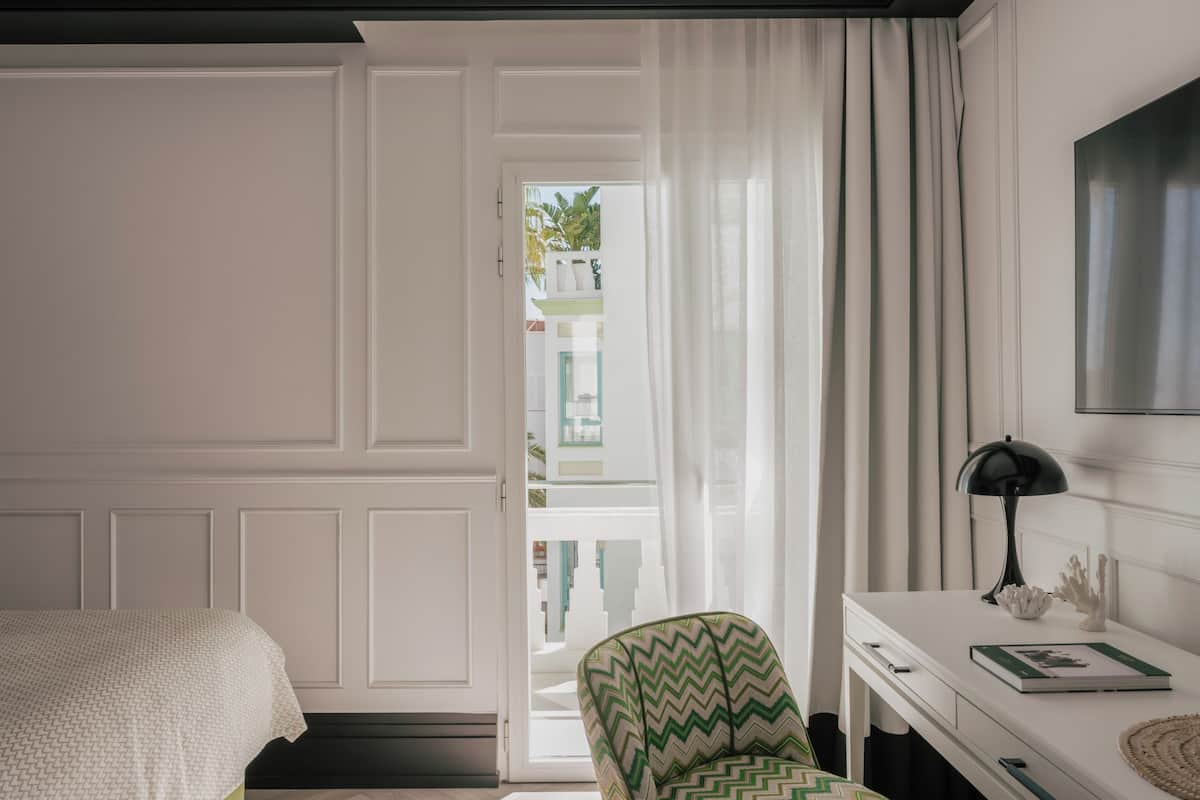 A bedroom with a bed, a chair, a desk, a lamp, and a view through a door.