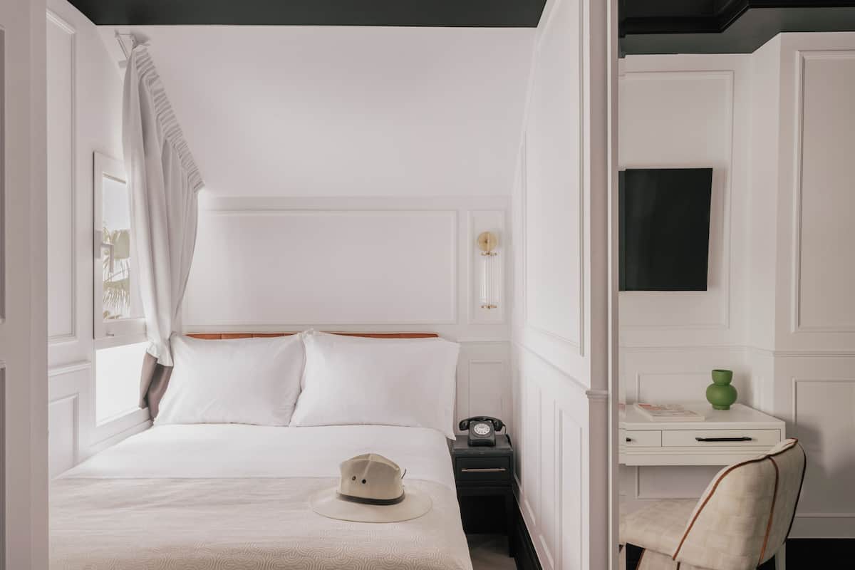 A hotel room with a bed, a desk, a chair, and a nightstand.