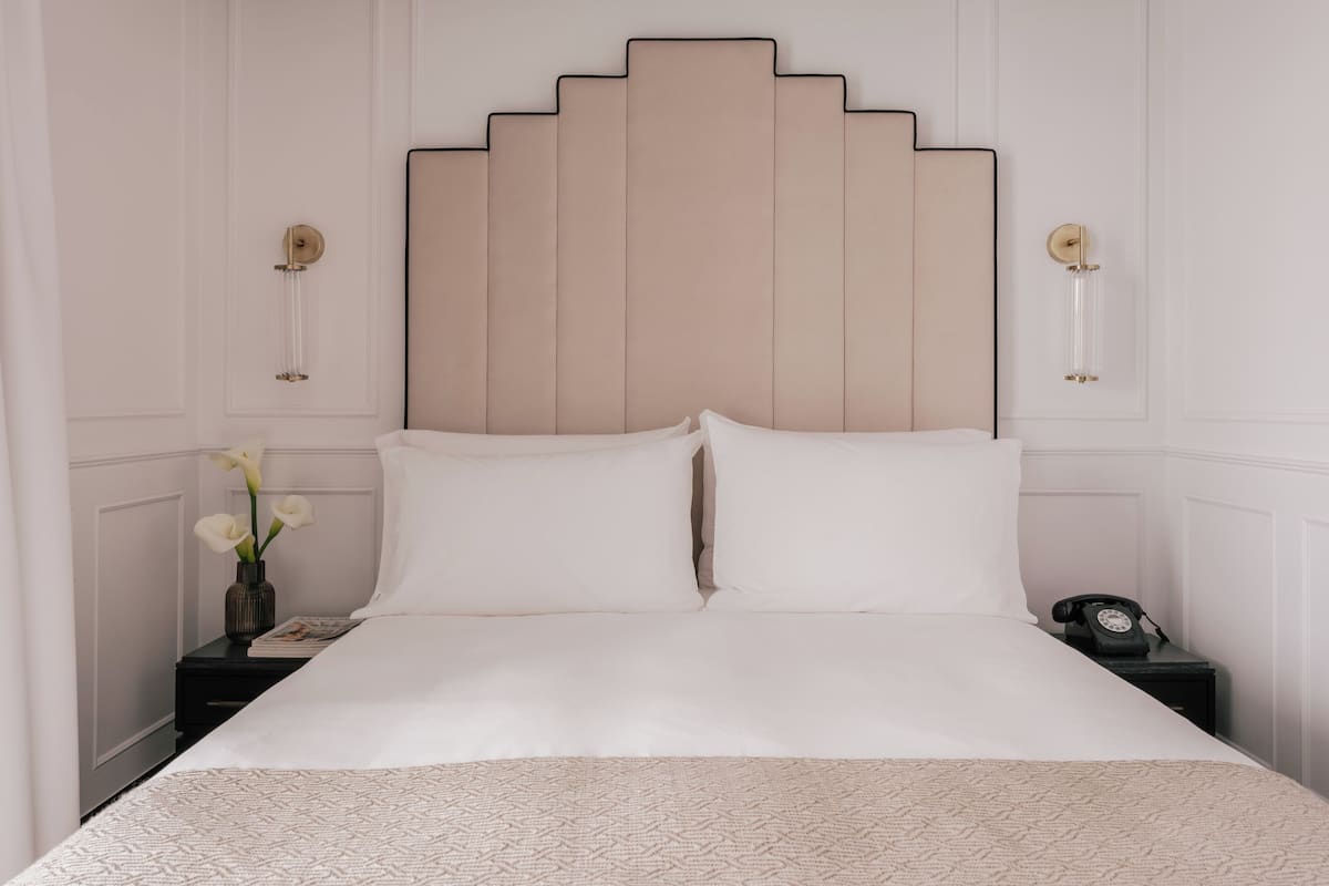 A bed with a headboard, two bedside tables, a vase with flowers, and a telephone on one of the tables.