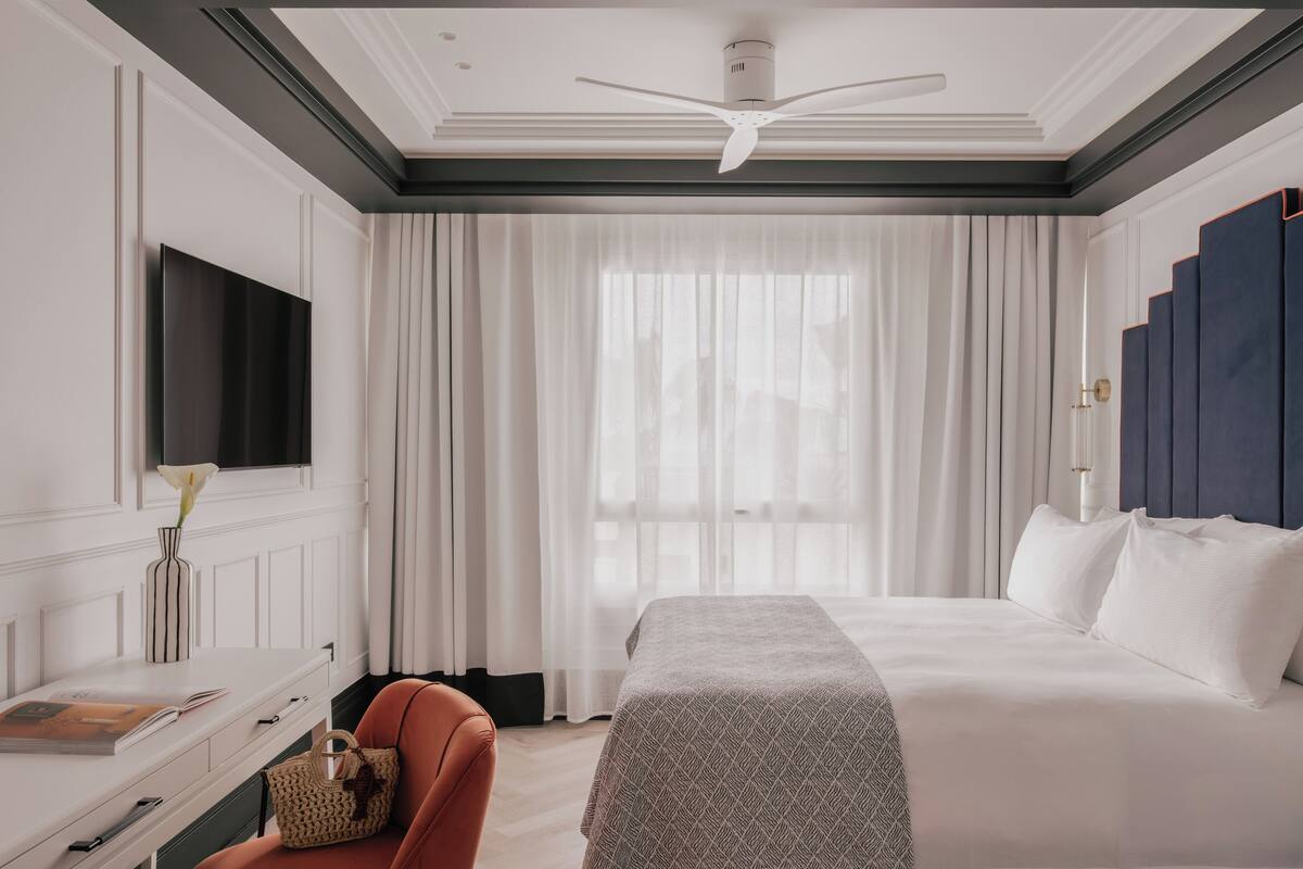 A hotel room with a bed, a desk, a chair, a television, and a window with curtains.