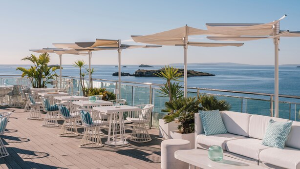 A rooftop terrace with outdoor seating, a white sofa, and a view of the sea.