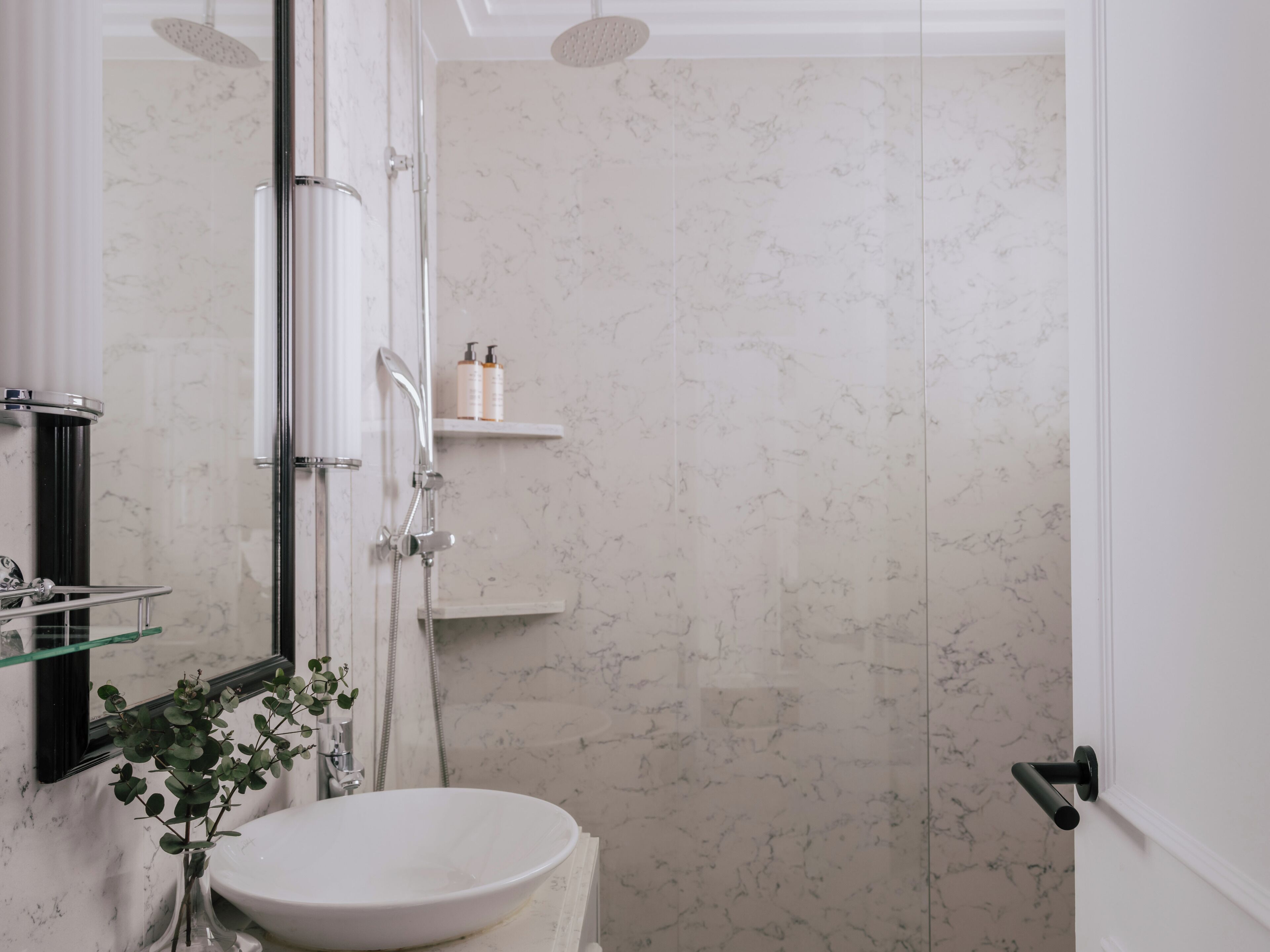 Une salle de bain avec une douche à parois de verre, un lavabo blanc et une petite étagère contenant des articles de toilette.