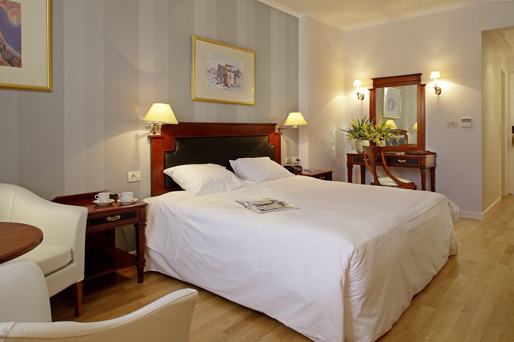 Una habitación de hotel con una cama grande, mesitas de noche, una silla, un escritorio y un espejo.