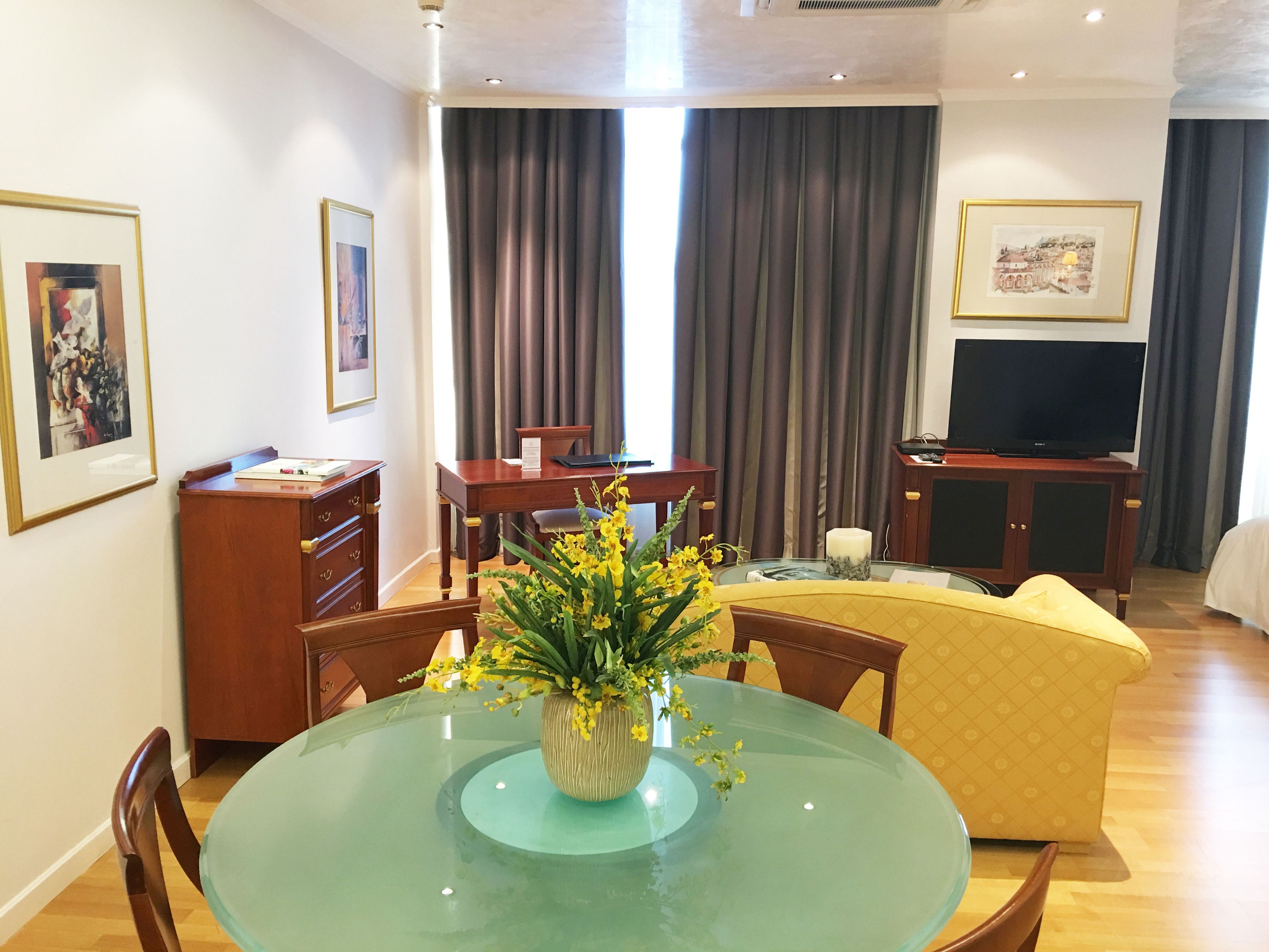 A hotel room with a dining table, chairs, a TV, and a bed.