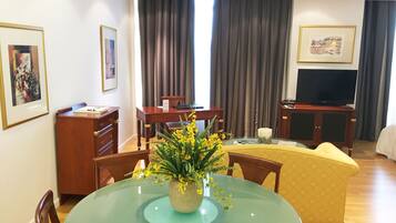 A hotel room with a dining table, chairs, a TV, and a bed.
