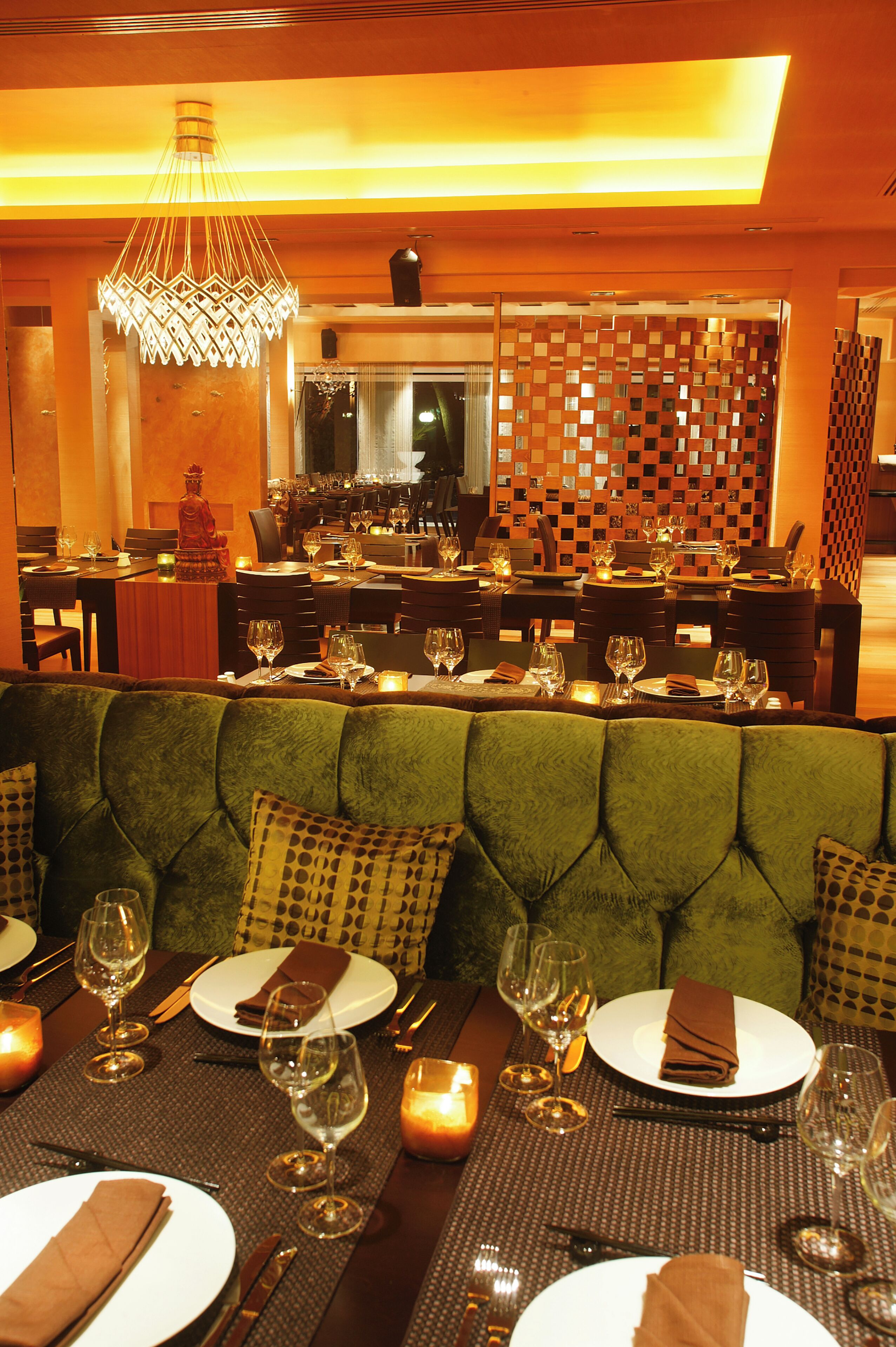 A restaurant with a green upholstered booth, tables set with wine glasses, plates, and cutlery.