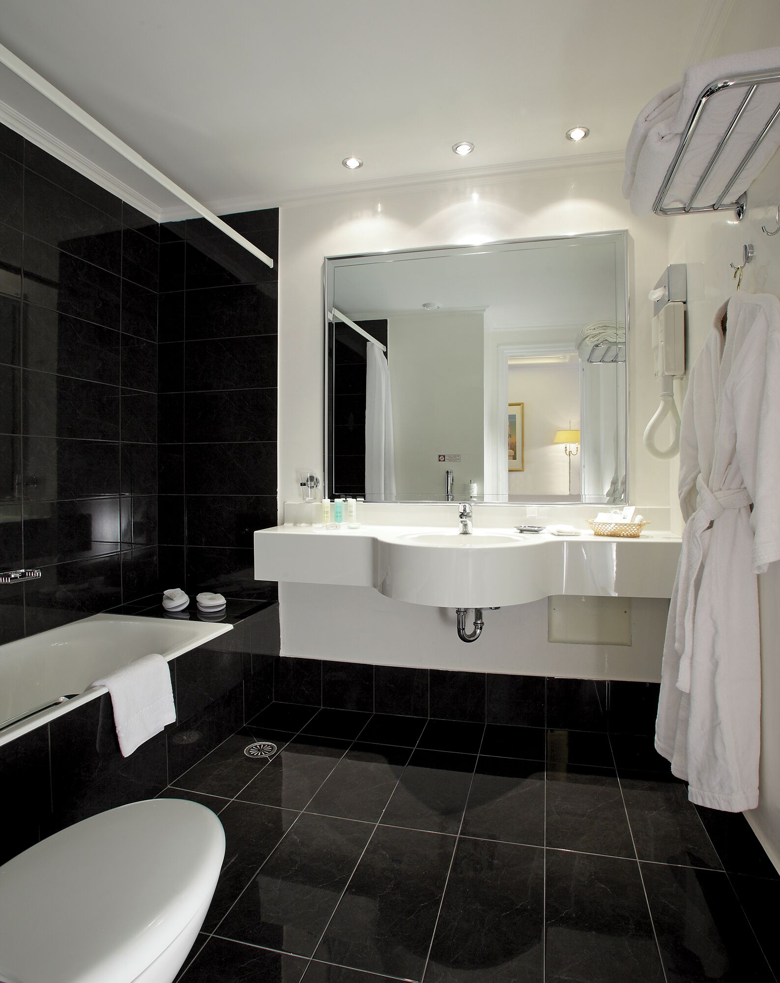 Une salle de bain moderne avec un grand miroir, deux lavabos, une baignoire et des toilettes.
