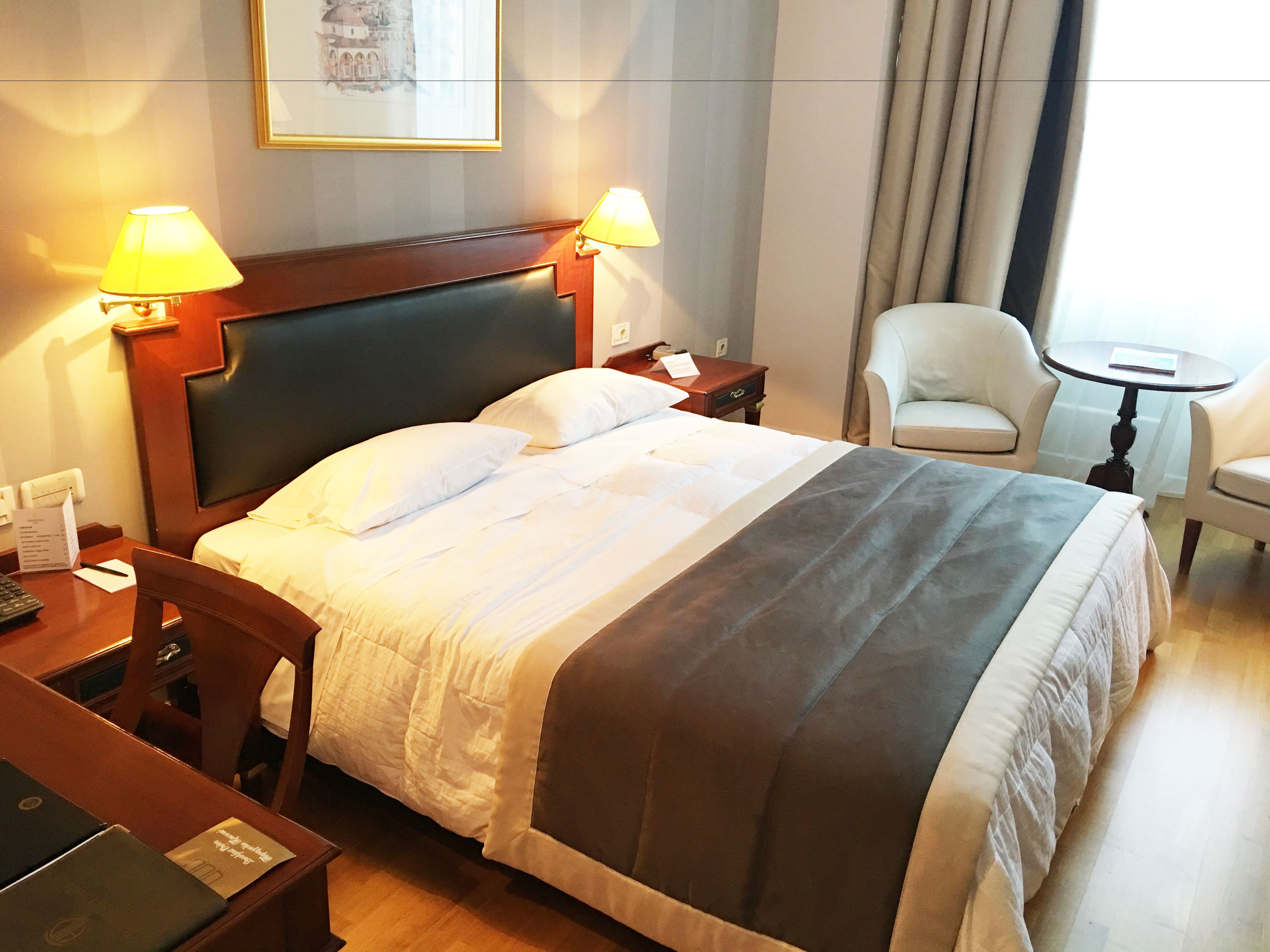 Une chambre d’hôtel avec un grand lit, deux lampes de chevet, une chaise, une petite table ronde et un bureau avec un ordinateur portable.