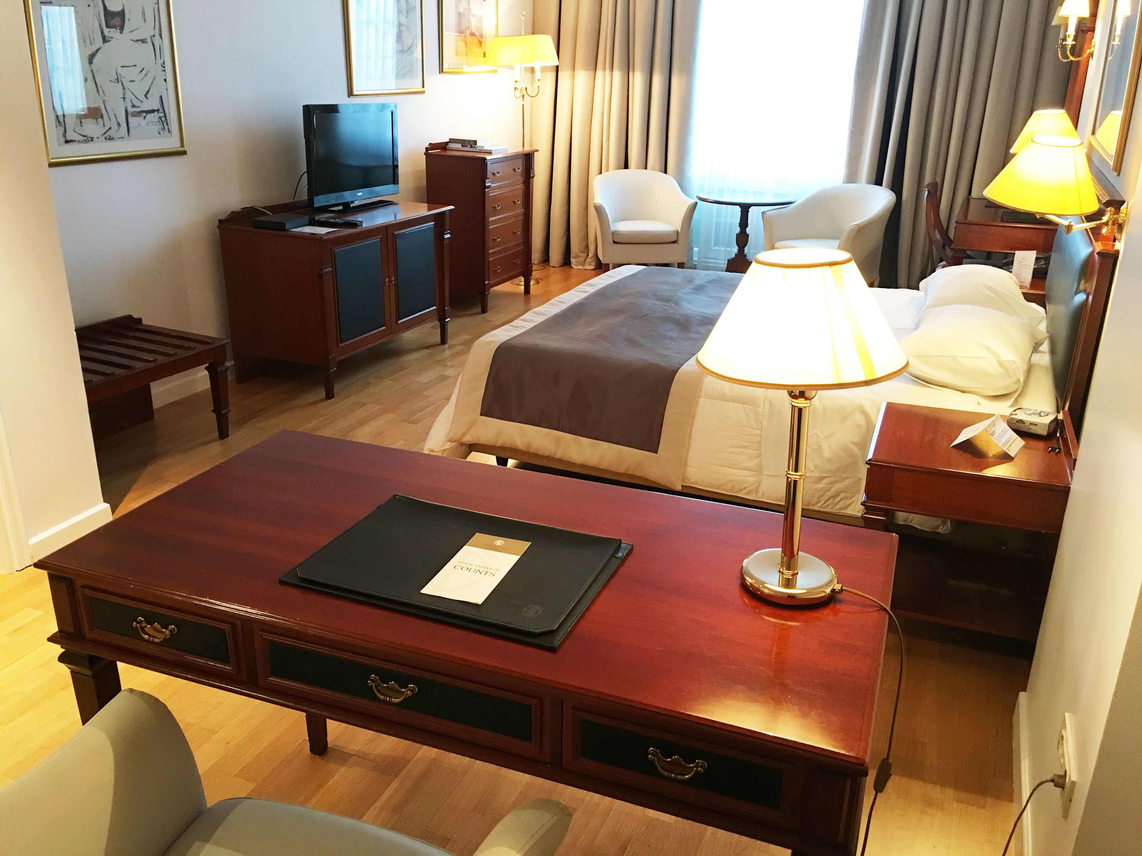 A hotel room with a bed, a desk, a chair, a television, and a lamp.