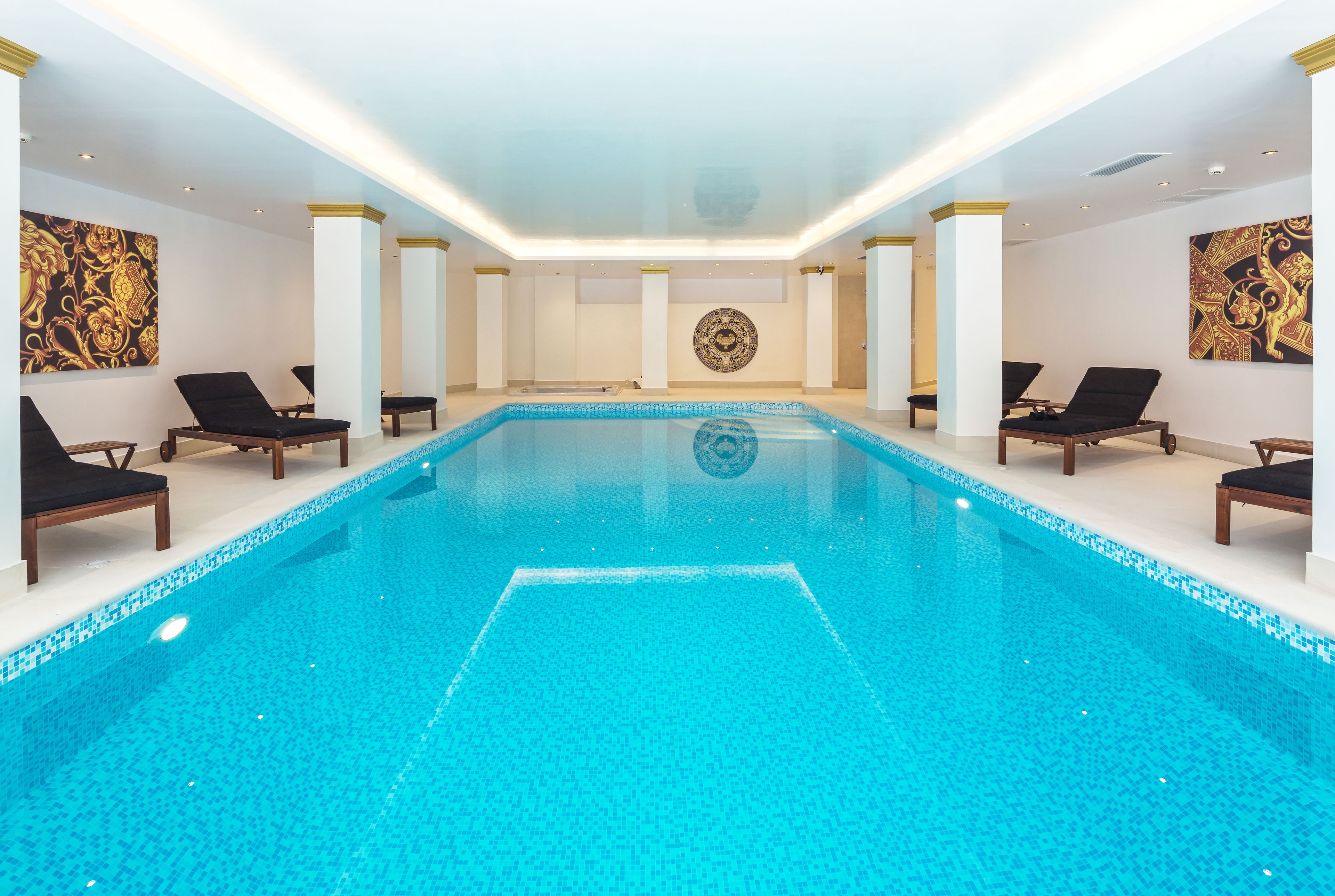 A large indoor swimming pool with black lounge chairs and a central decorative wall.
