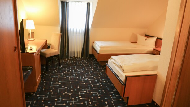 Une chambre d’hôtel avec deux lits, un bureau avec une lampe, une chaise et une fenêtre avec des rideaux.
