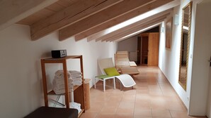 A hallway with a wooden bench, a chair with a green cushion, and a shelf with folded towels. - Hotel Königer (Pliening)