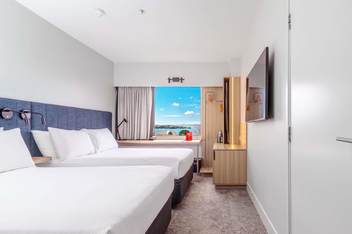 Habitación de hotel con dos camas, televisión, escritorio y vista al mar.