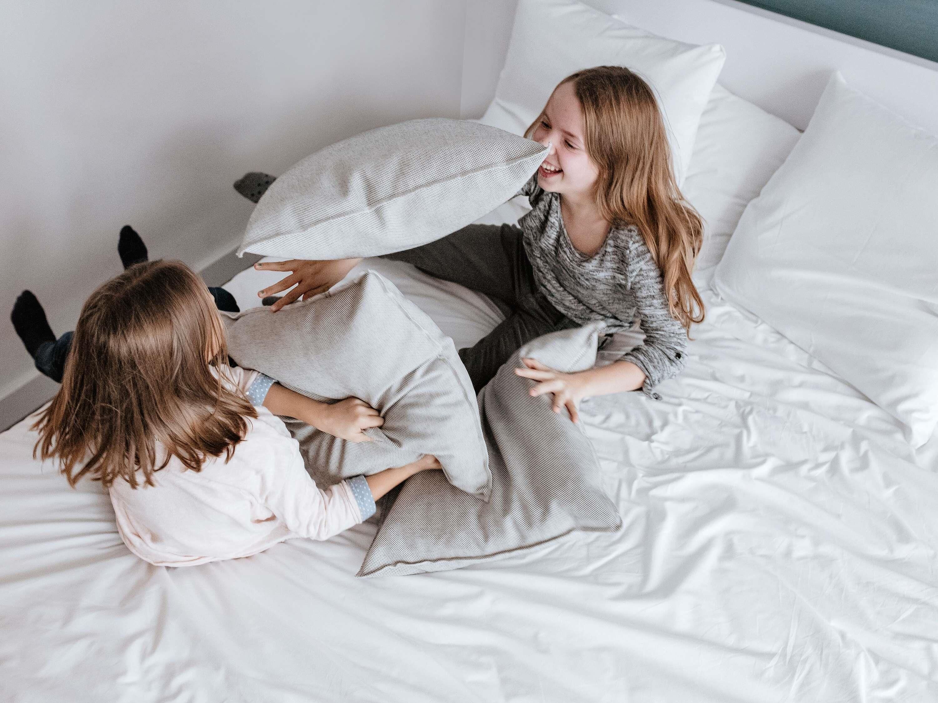 A bed with white bedding and pillows, a person sitting on the bed, and another person lying down.