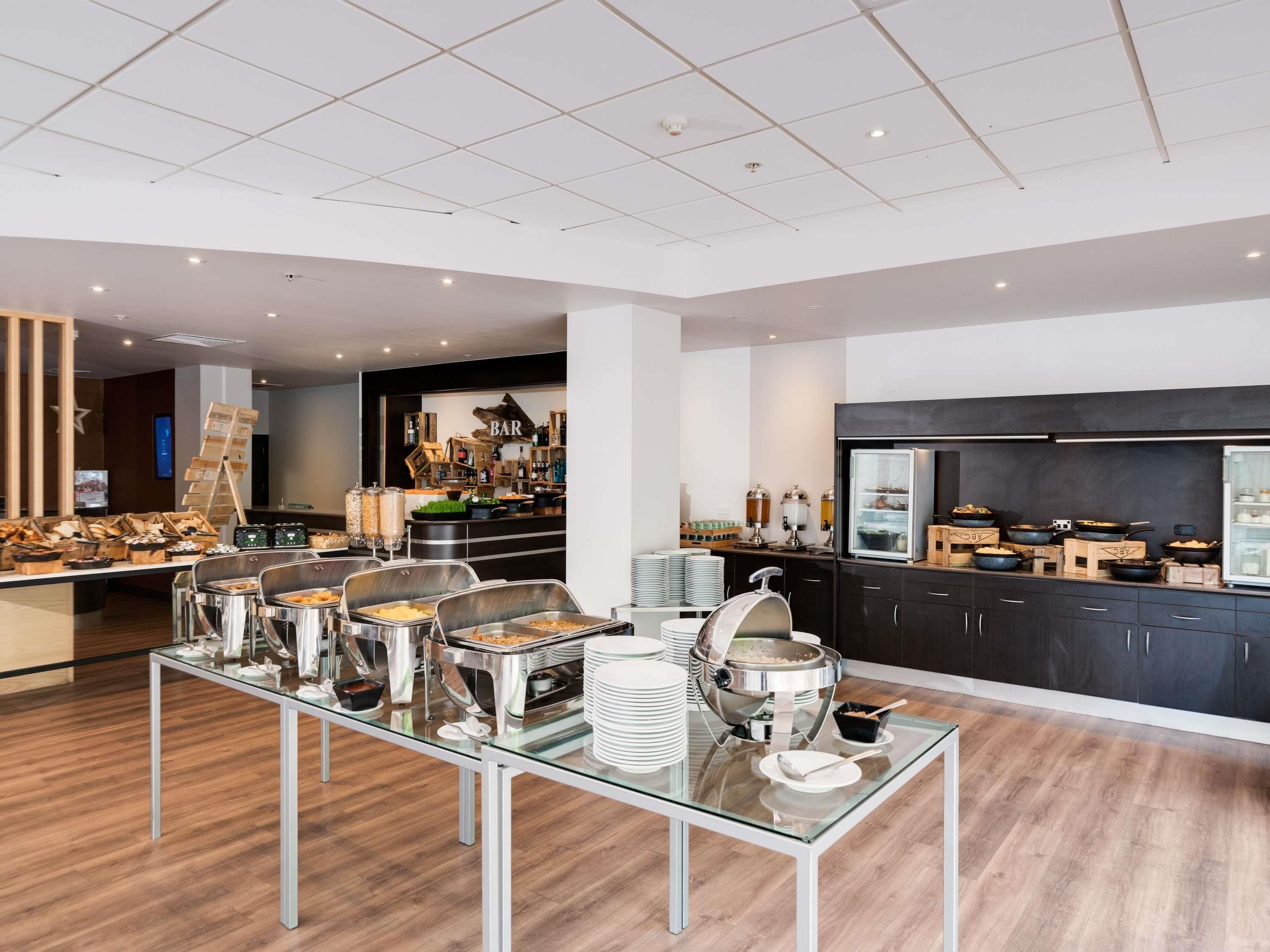 A modern buffet setup with multiple serving stations, a bar area, and a kitchen in the background.