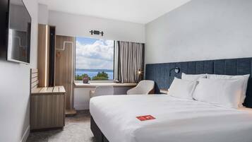 A hotel room with a bed, desk, chair, and a view of the outdoors.