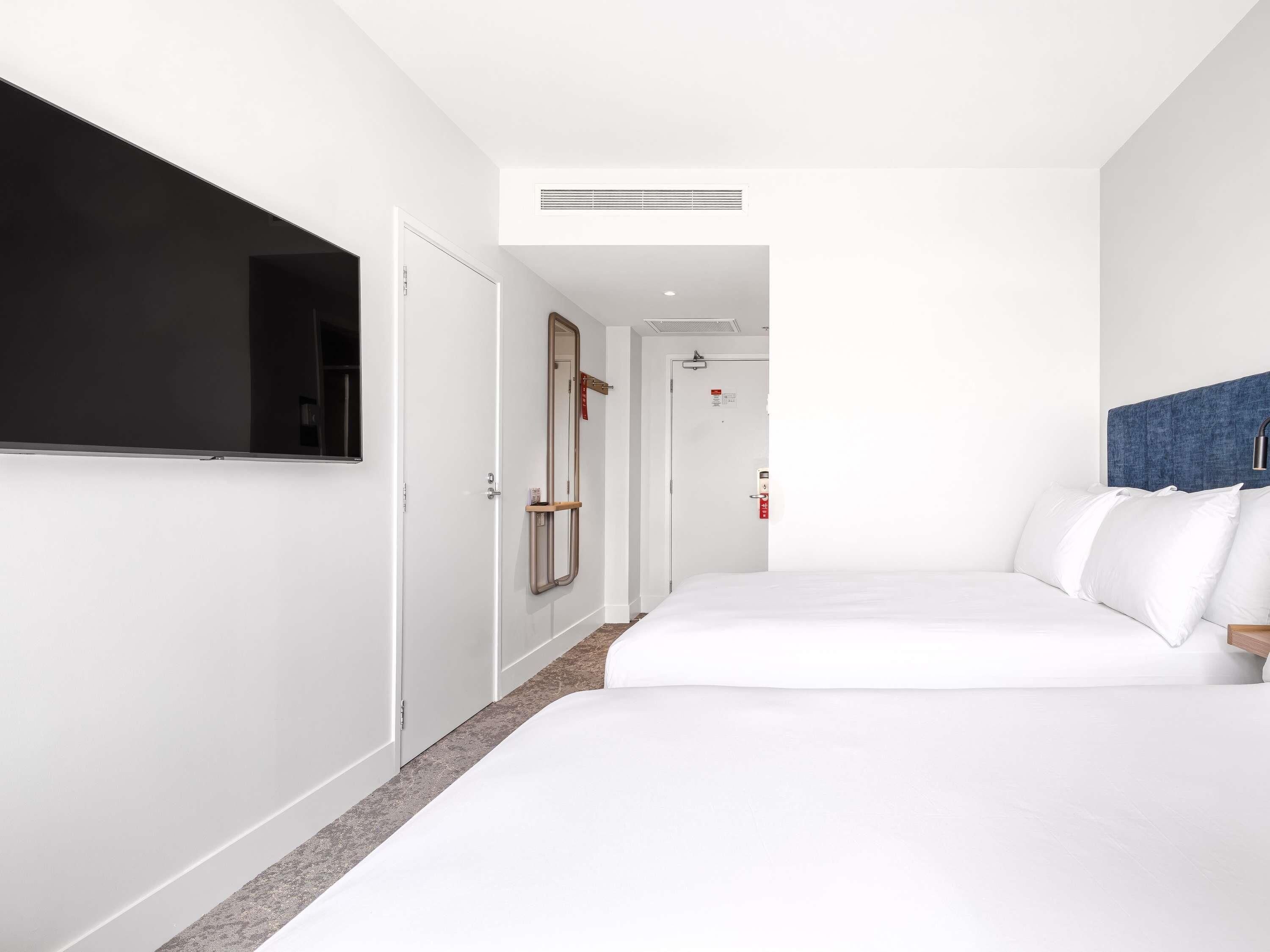 A hotel room with a bed, a television, a door, and a mirror.