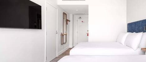 A hotel room with a bed, a television, a door, and a mirror.