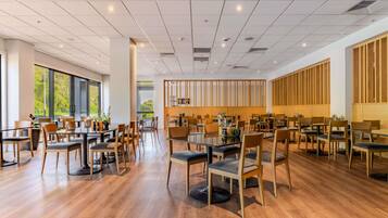 Un vaste espace dédié à la salle à manger, avec de nombreuses tables et chaises, de grandes fenêtres et un design moderne au niveau du plafond.