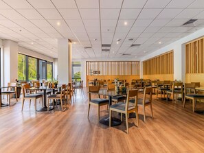 A spacious dining area with multiple tables and chairs, large windows, and a modern ceiling design.