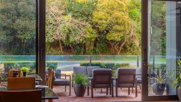 A modern interior with a glass door leading to a garden view, featuring a seating area with chairs and a table, and potted plants.
