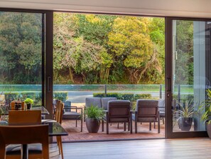 A modern interior with a glass door leading to a garden view, featuring a seating area with chairs and a table, and potted plants.