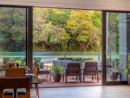 A modern interior with a glass door leading to a garden view, featuring a seating area with chairs and a table, and potted plants.