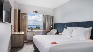 A hotel room with a bed, desk, chair, and a view of the outdoors.