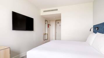 A hotel room with a bed, a television mounted on the wall, a door, and a small bedside table.